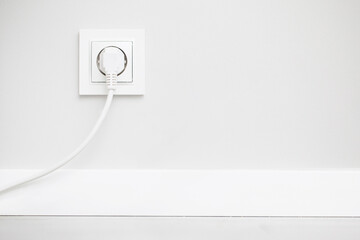 Electrical socket isolated on gray wall. White wire plug plugged in. Renovated studio apartment...