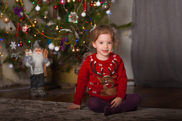 Little girl child in red Christmas sweater for New Year at home...