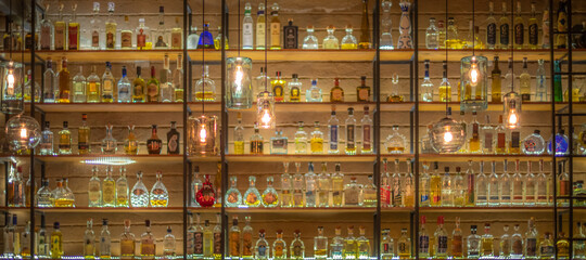 Defocused background of bar counter with various bottles of alcohol. - obrazy, fototapety, plakaty