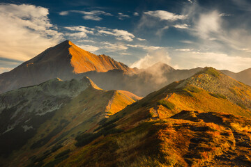 Beautiful autumn in the Western Tatras. Yellow and orange grasses create an amazing atmosphere. The light of the setting sun illuminates the mountain ridges.