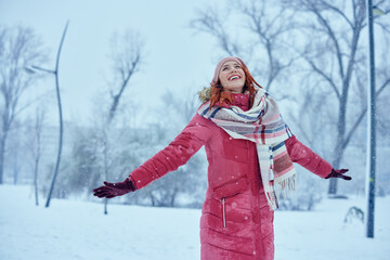 Fototapeta na wymiar Happy young woman enjoys snowfall in park
