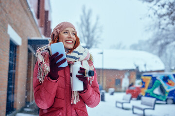 Woman using phone and drinking hot beverage outdoors