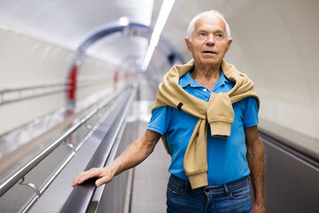 Positive mature man walking down escalator to subway station platform