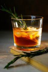 Whiskey sour cocktail with rum ice and rosemary in shot glass on book. Alcohol cocktail in light beam