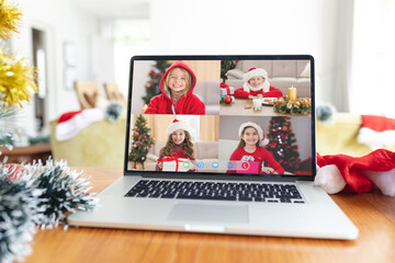 Happy caucasian girls in santa hats smiling on laptop group video call screen at christmas time