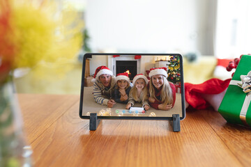Happy caucasian family in santa hats smiling on tablet video call screen at christmas time