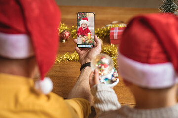 Father and son in santa hats making christmas smartphone video call with excited caucasian boy
