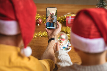 Father and son in santa hats making christmas smartphone video call with african american couple