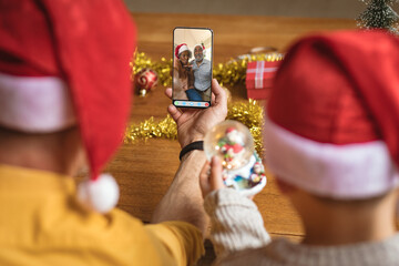 Father and son in santa hats making christmas smartphone video call with african american couple