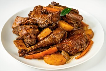 Many pieces of baked hen with carrot, pear and spices on plate.