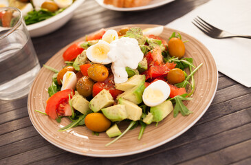 fresh salad of arugula, avocado, cherry tomatoes with olives and quail eggs on brown plate