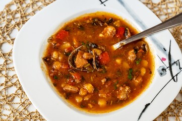 Spicy soup with pork meat, red pepper, bean and mushroom in plate.