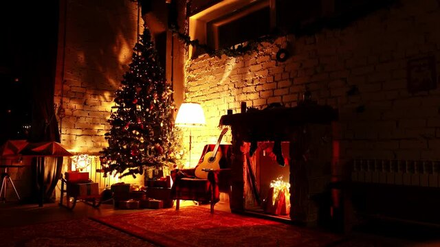 Warm atmosphere of Christmas interior in house with festive tree spruce and fake fireplace in loop. New Year's cozy interior with beautiful fir decorated by garlands and presents lying under it.