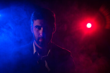 Photo of man looking at camera on dark background with pink and blue lights.