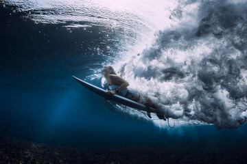 Surfer woman with surfboard duck dive under wave in tropical ocean.
