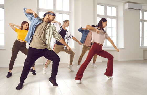 Happy young dancers group in casual clothes practice in studio. Smiling millennial people dance perform prepare for concert together. Hobby and entertainment concept. Professional dancing session.