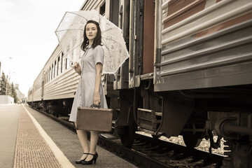 A confident, statuesque, elegant young woman with an umbrella and a vintage suitcase in her hands got off the train. Traveling by train.Business lady, retro style