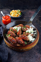 Traditionelle kroatische Cevapi als würzige Fleischbällchen mit scharfem Ajvar und Kraut Karotten Salat serviert als close-up in einer rustikalen Bratpfanne 