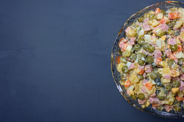 Olivier salad in crystal bowl on blue background, copy space