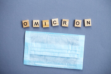 word omicron made by wooden blocks with medical mask on gray background.