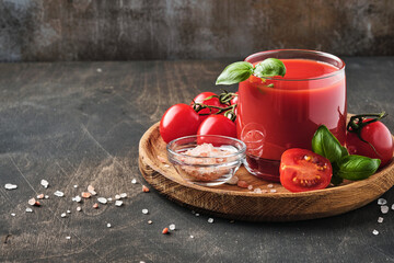 Glass of fresh tomato juice, salt, basil and tomatoes on  wooden stand  on old wooden background. With copy space.