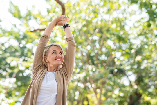 Portrait photo of happy senior Caucasian woman relaxing and breathing fresh air with sunlight in outdoors park. Elderly woman enjoying a day in the park on summer. Healthcare lifestyle and wellness	