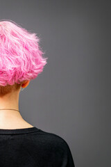 Back of female head with curly short pink hair against the dark background