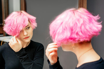Beautiful young caucasian woman looking at her short pink hair in a mirror