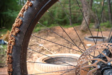 Dirty disc brake front wheel of a mountain bike on a trail in the forest with old car tires in the background