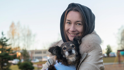 Obraz premium Beautiful girl hugs cute little dog after visits vet. A girl walks on the street with a small dog after surgery.