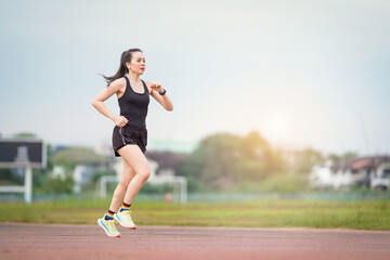 Fototapeta na wymiar A mature Asian woman athlete runner jogging in city stadium in the sunny morning to keep fitness and healthy lifestyle. Active healthy runner jogging outdoor
