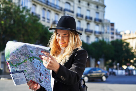 Young positive woman in black hat exploring map of city