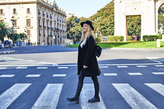 Smiling woman in coat and hat walking on zebra crossing