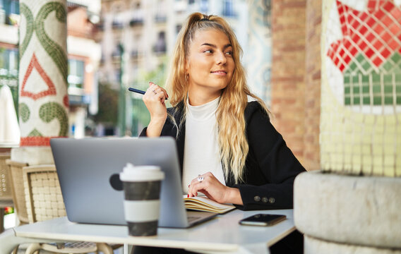 Freelancer woman writing notes while working with laptop in cafe