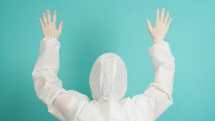 Back of a woman who wears a PPE suit is rise hand up on a mint or Tiffany Blue background.