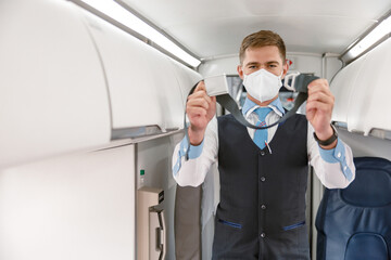 Fototapeta na wymiar Male flight attendant in medical mask holding seatbelt