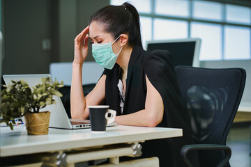 Businesswoman wearing facial mask and has headaches in office