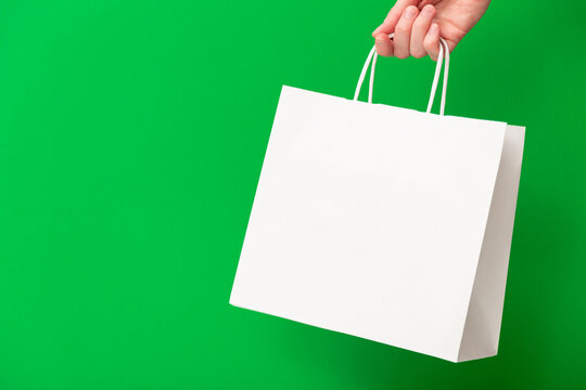 Female hand holding white blank shopping bag isolated on green background. Black friday sale, discount, recycling, shopping and ecology concept.