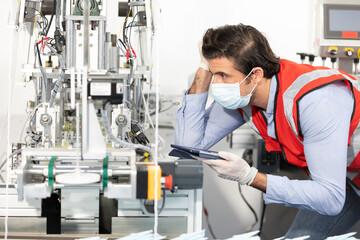 male factory worker holding tablet computer and operating machine in factory