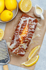 Homemade pound cake loaf with lemon glaze and zest on baking paper on a gray concrete background. Fresh citrus pastries. Selective focus
