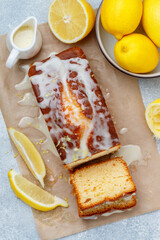 Homemade pound cake loaf with lemon glaze and zest on baking paper on a gray concrete background. Fresh citrus pastries. Selective focus