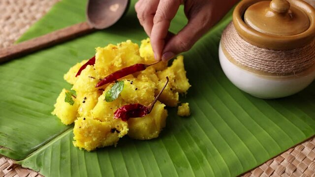 Cooked tapioca or Cassava root Mandioca Aipim  Kappa Indian food woman hand serving on banana leaf 4K video footage. South Indian food served with meat fish curry Asian cuisine  Kerala India Sri Lanka