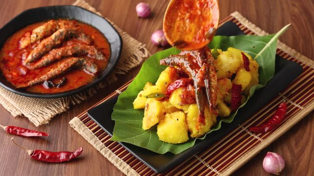 tapioca spicy hot Kerala fish curry woman hand serving Indian food banana leaf 4K video footage. Kappa sardine masala fish curry Asian cuisine Bengali macher Jhal Goan fish curry coconut milk cassava 
