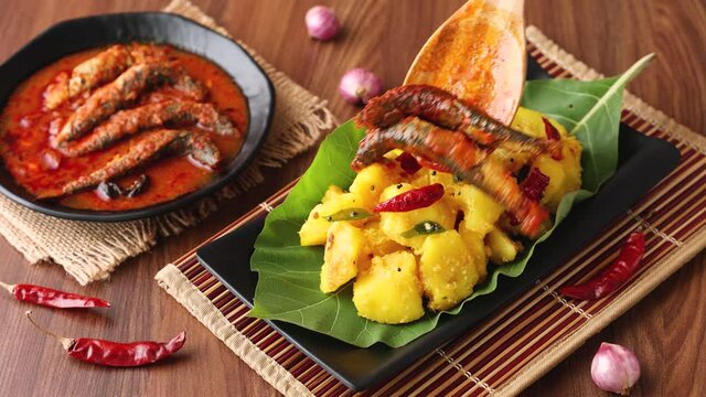 tapioca spicy hot Kerala fish curry woman hand serving Indian food banana leaf 4K video footage. Kappa sardine masala fish curry Asian cuisine Bengali macher Jhal Goan fish curry coconut milk cassava 