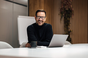 Portrait of smiling caucasian man using his laptop in office.