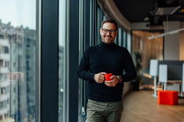 Portrait of happy adult man, holding a cup of tea and smiling near the window.