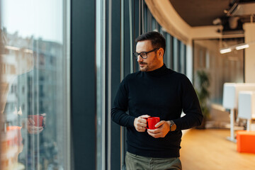 Thoughtful adult man, holding a cup of coffee while gazing through the window.