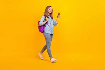 Fototapeta na wymiar Full length profile photo of funky teen girl go look telephone wear bag jeans shirt footwear isolated on yellow background