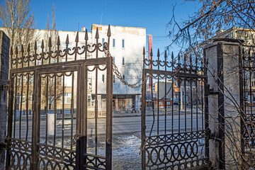 View through the half-open gates of the city park to the street on a sunny winter day