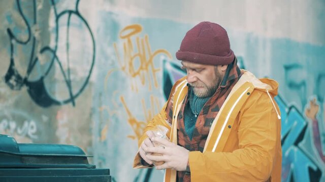 A homeless man is eating food from a trash bin